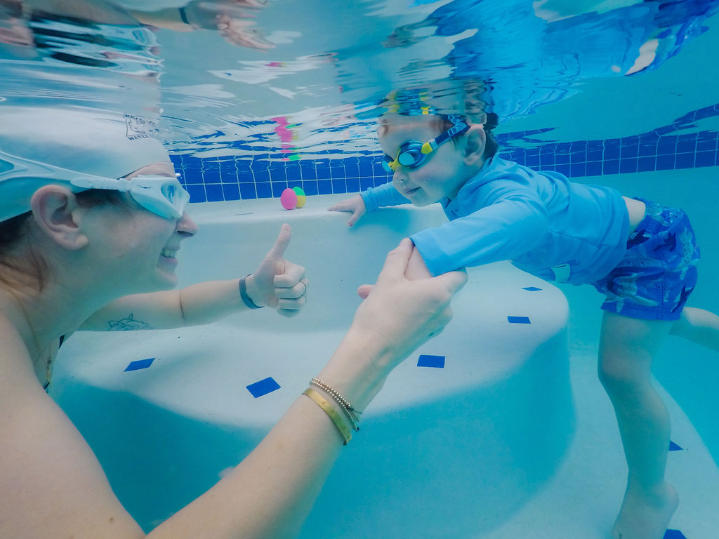 Instructor giving thumbs-up to a young swimmer underwater