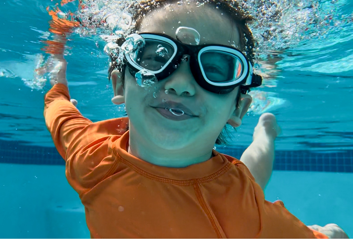 Young swimmer underwater wearing an orange rash guard