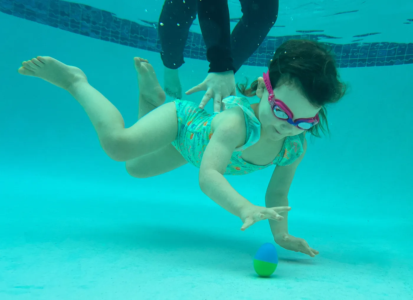 Young swimmer diving underwater to reach a toy egg