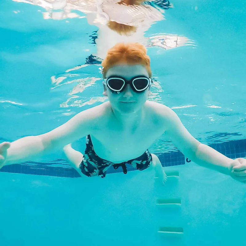 Older swimmer underwater with goggles, arms outstretched mid-swim