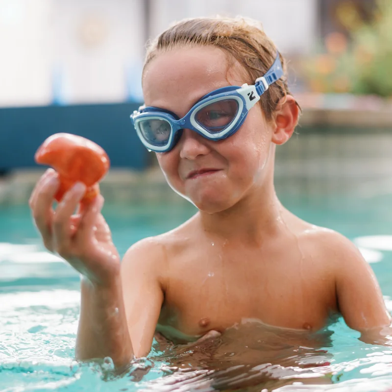 Young swimmer with goggles holding a colorful pool toy, smiling with their instructor